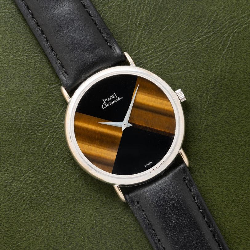 A Piaget Tigers Eye Onyx Dress Watch with a black and gold striped face and black leather strap rests on a green leather surface.