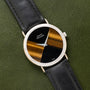 A Piaget Tigers Eye Onyx Dress Watch with a black and gold striped face and black leather strap rests on a green leather surface.