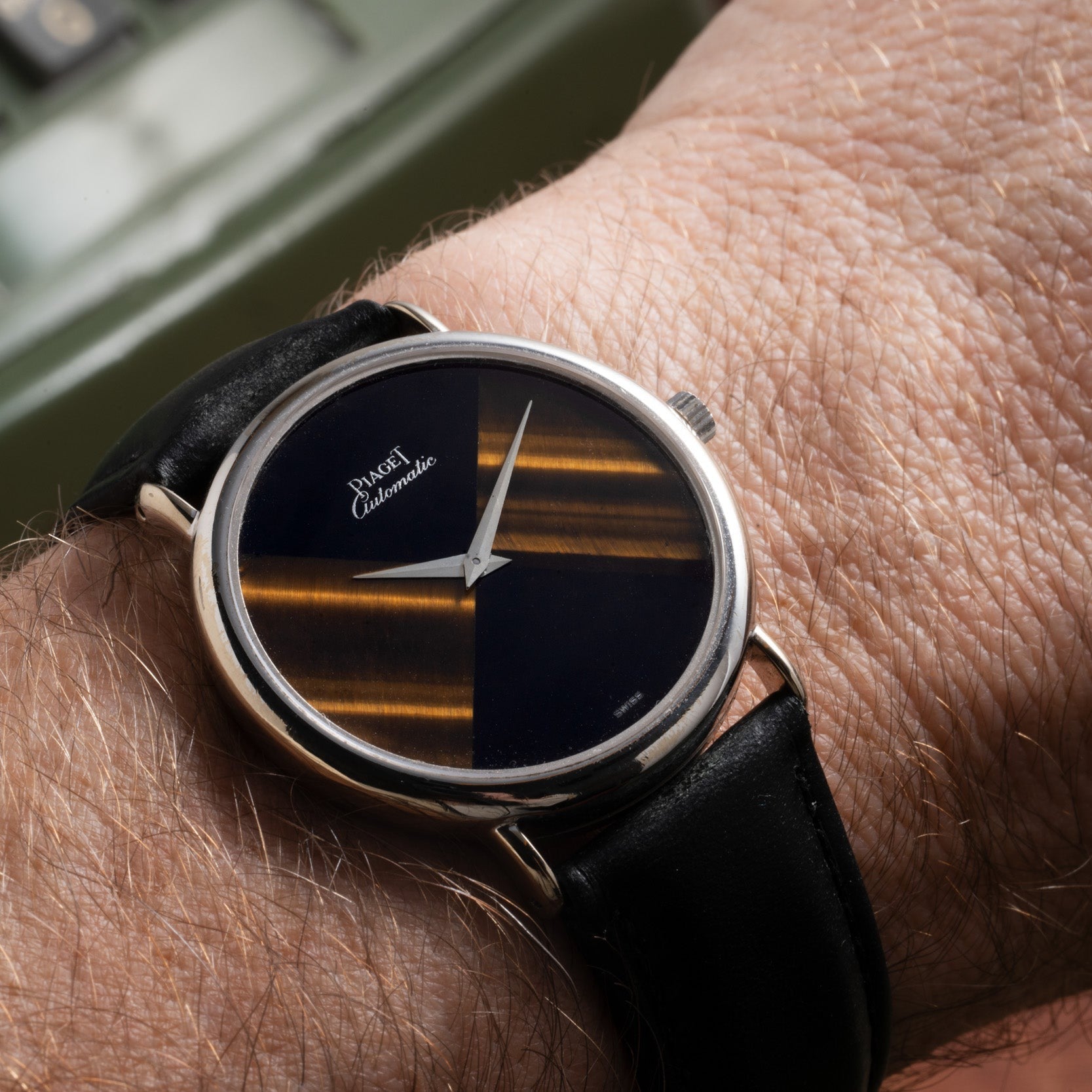 A close-up of a Piaget Tigers Eye Onyx Dress Watch with a black and gold face on a persons wrist.