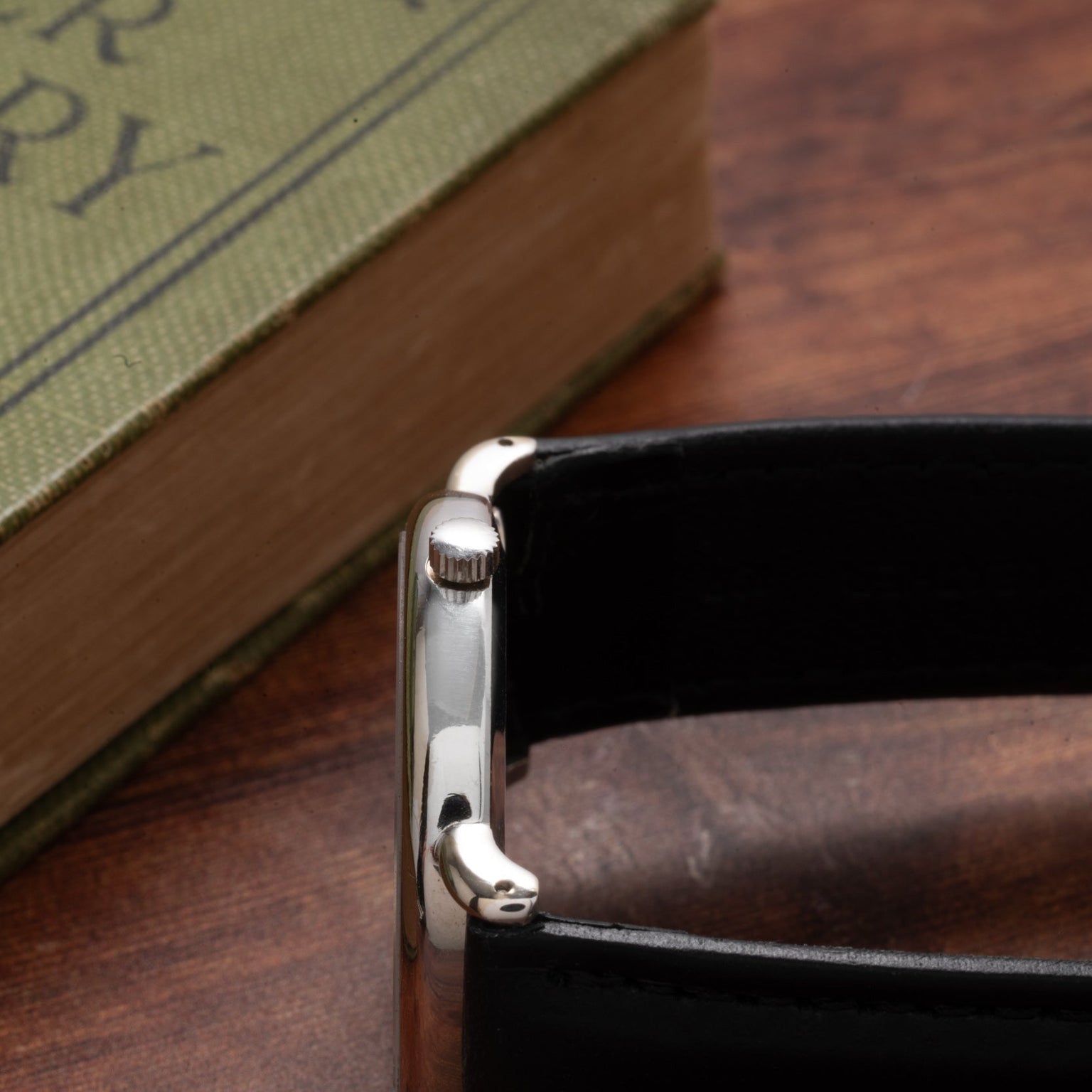 A close-up of the Piaget Tigers Eye Onyx Dress Watch with a black strap, placed beside a green book on a wooden surface.