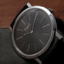 A close-up of the Piaget Altiplano wristwatch, featuring a black dial with silver hour markers and a black leather strap.