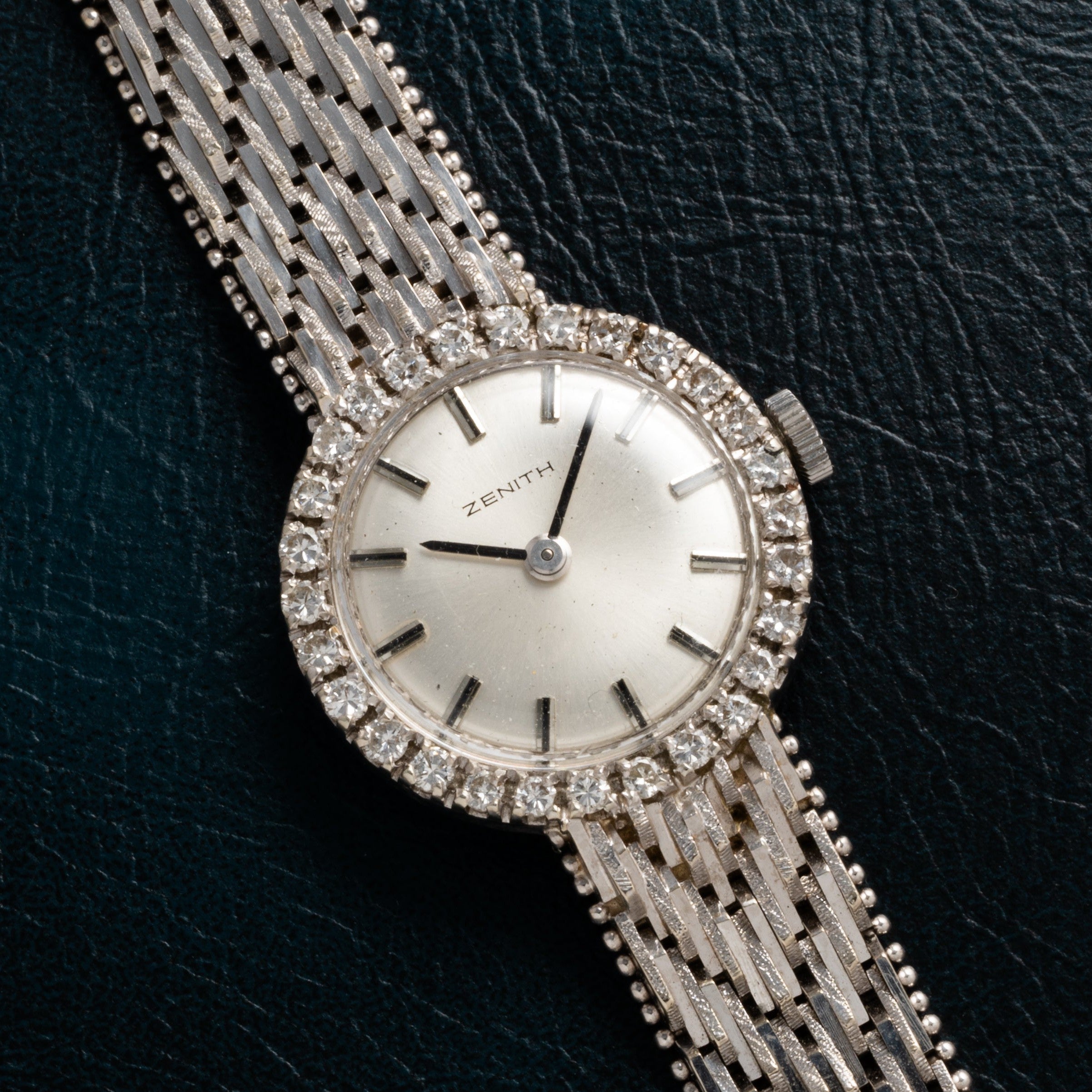 The Ladies Cocktail Watch by Zenith features a diamond-encrusted bezel and textured metal band, displayed on a dark surface.