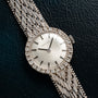 The Ladies Cocktail Watch by Zenith features a diamond-encrusted bezel and textured metal band, displayed on a dark surface.