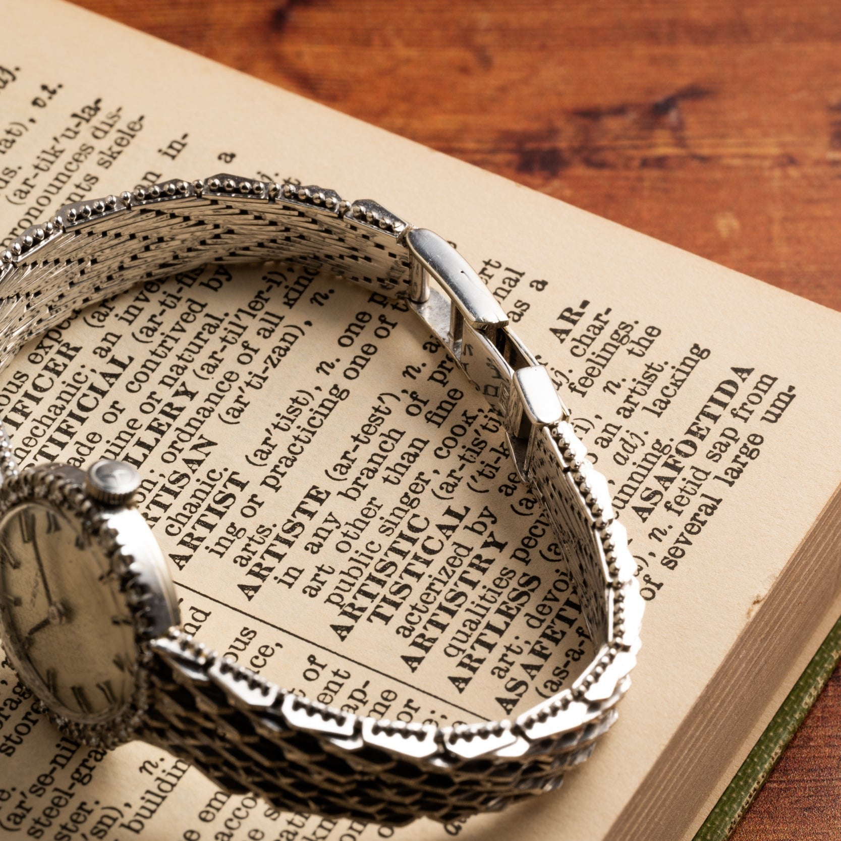 A Zenith Ladies Cocktail Watch lies on an open dictionary displaying the definition of artistic.