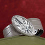 Cartier Libre Hypnose watch with diamond bezel and Roman numerals, displayed on a green surface against a red background.