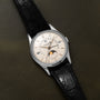 Patek Philippe Retrograde Perpetual Calendar: silver wristwatch with black leather strap, moon phase display, and date indicators on a dark leather surface.