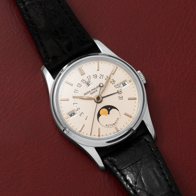 The Patek Philippe Retrograde Perpetual Calendar, featuring a black leather strap and moon phase display, is elegantly displayed on a red textured surface.