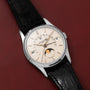 The Patek Philippe Retrograde Perpetual Calendar, featuring a black leather strap and moon phase display, is elegantly displayed on a red textured surface.
