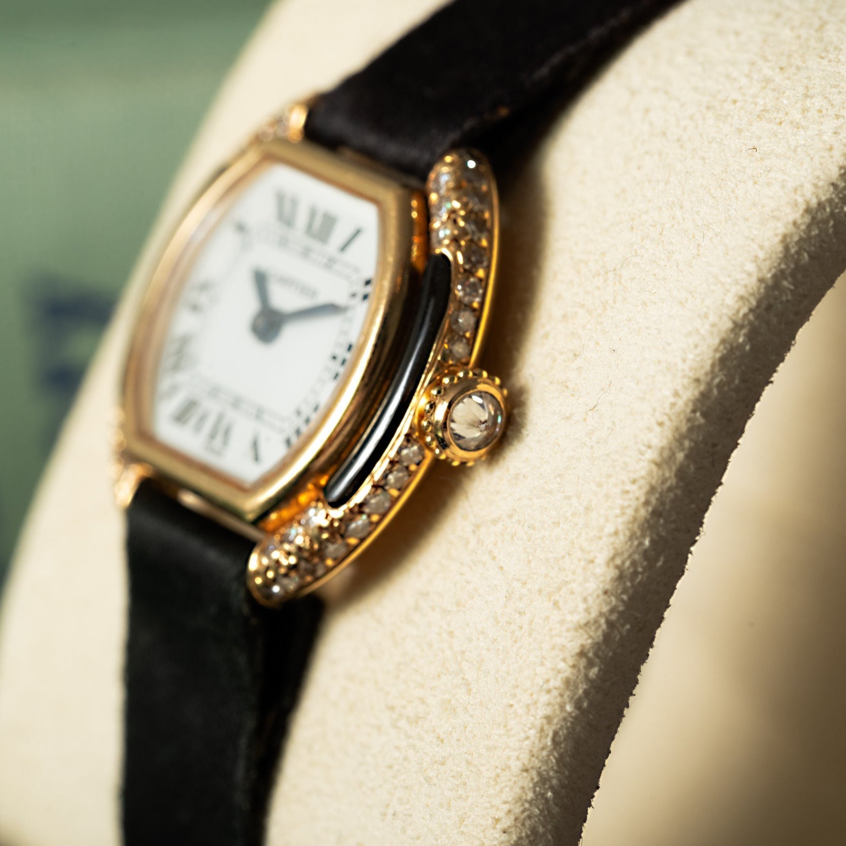Close-up of the Cartier Ellipse, a luxury gold watch featuring diamond accents and a black leather strap, presented on a cream display cushion.