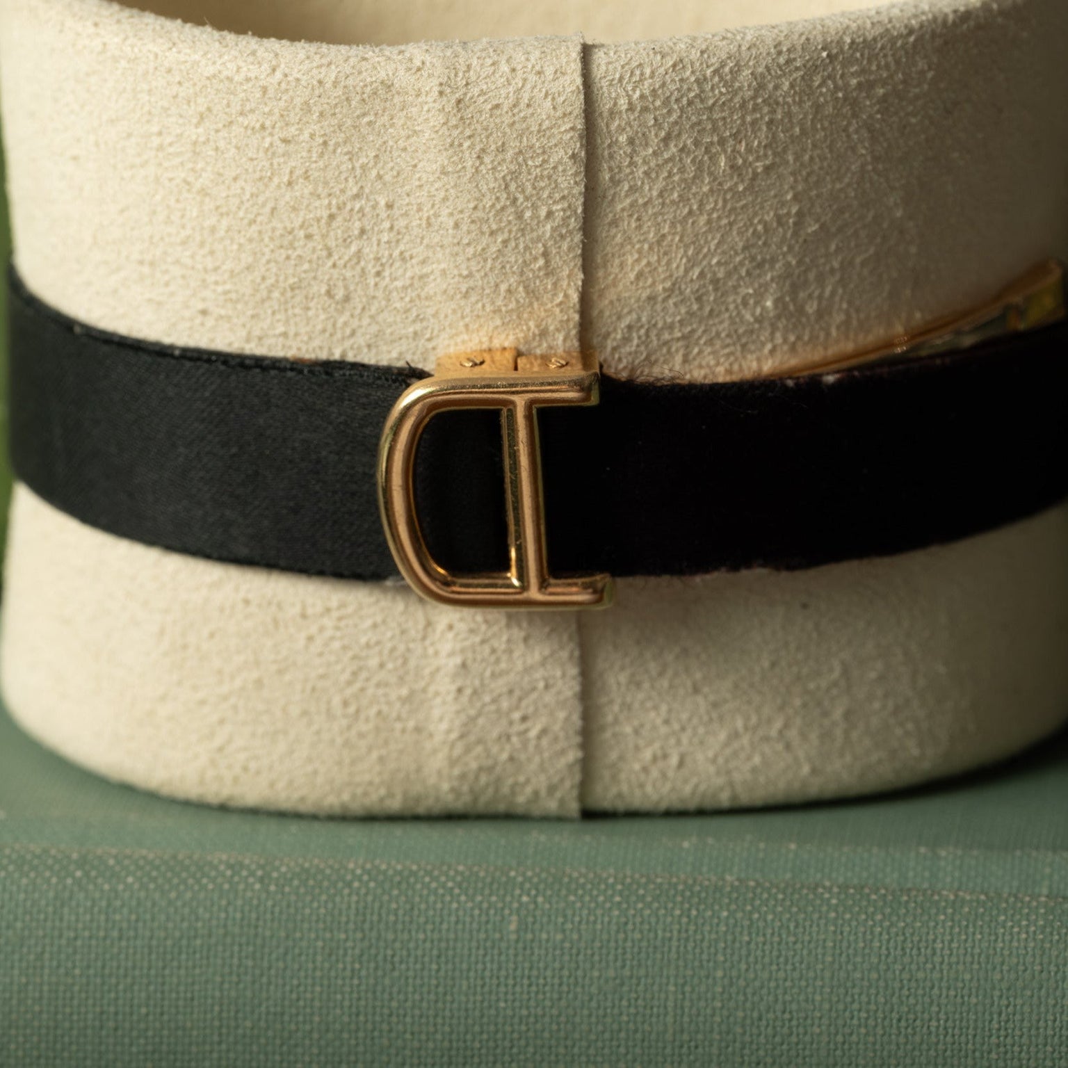 The Cartier Ellipse is a black choker with a gold D-shaped buckle, elegantly displayed on a beige stand.