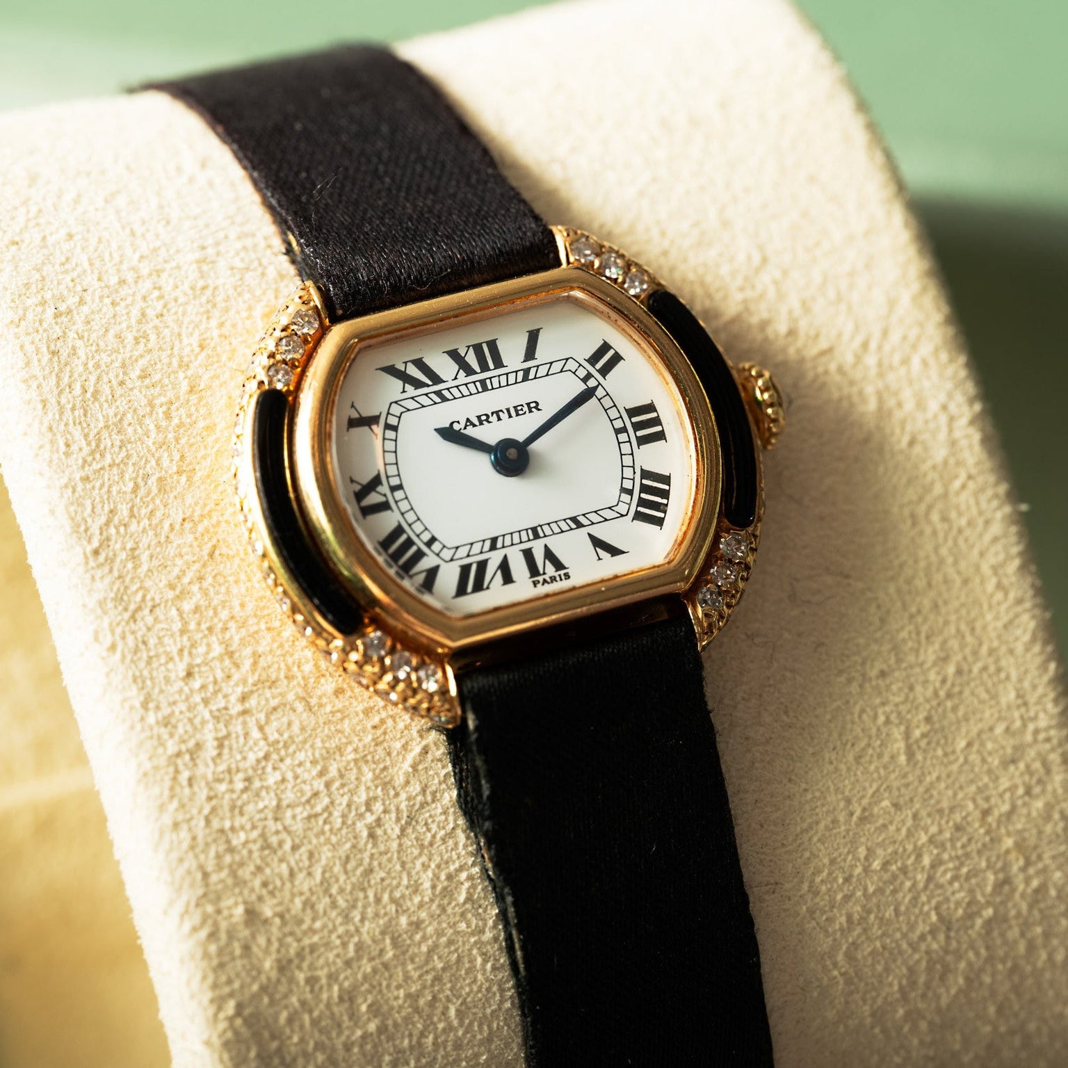 The Cartier Ellipse watch features a black strap and Roman numeral face, elegantly displayed on a beige cushion.