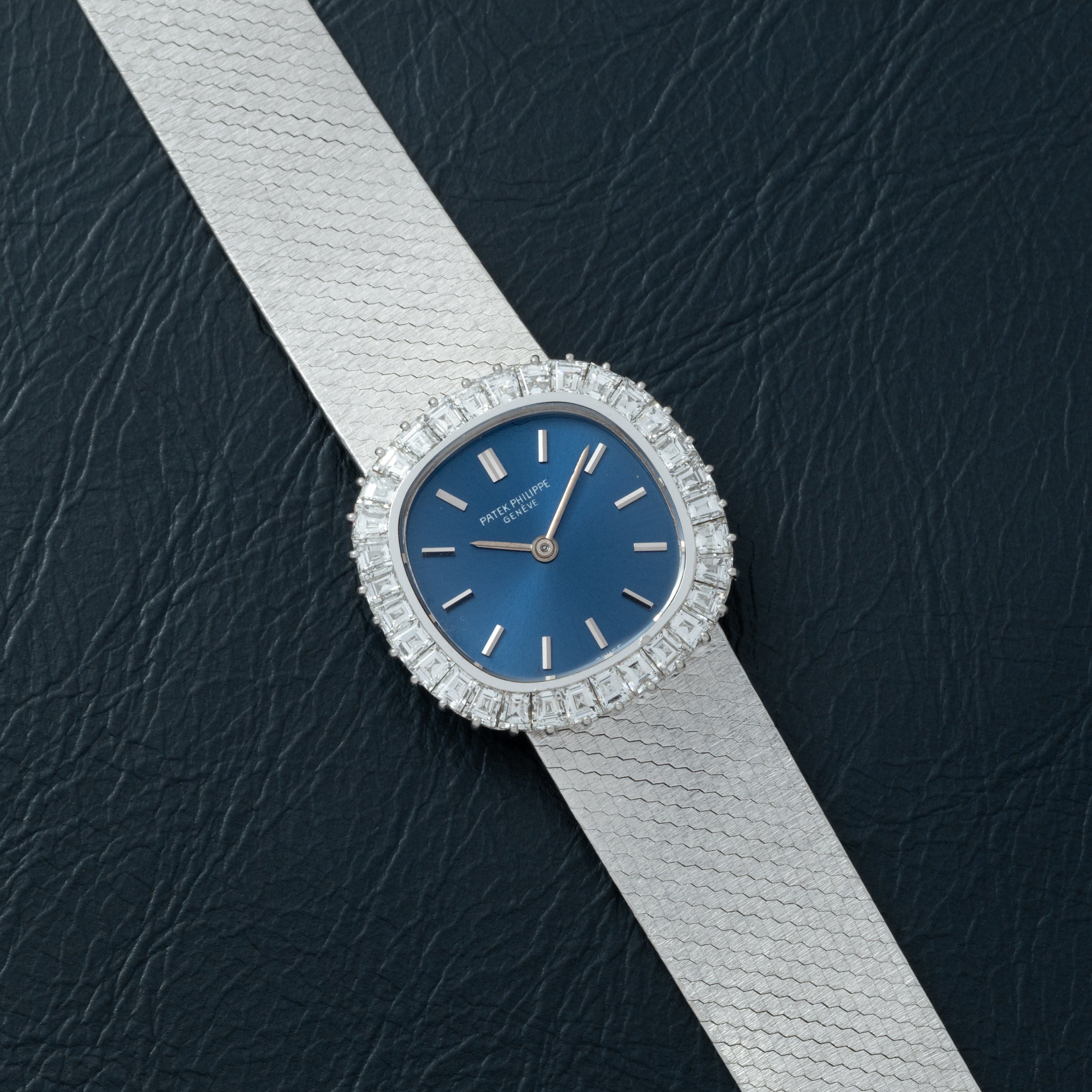 The Patek Philippe Ellipse Ladies Dress Watch features a silver case, blue face, and diamond bezel, elegantly displayed on black textured leather.