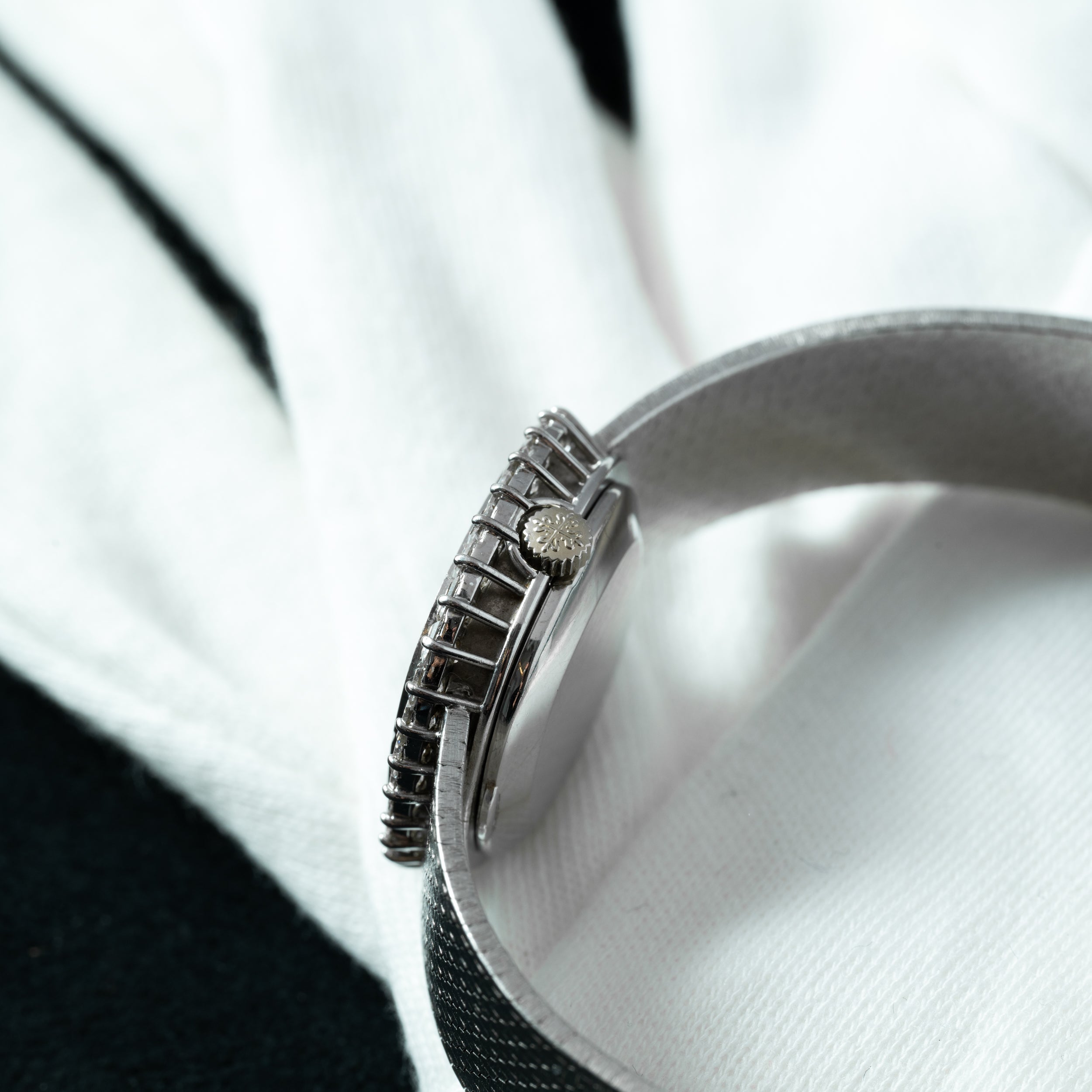 Close-up of the Patek Philippe Ellipse Ladies Dress Watch with a silver metal band, shown on a white and black fabric background.
