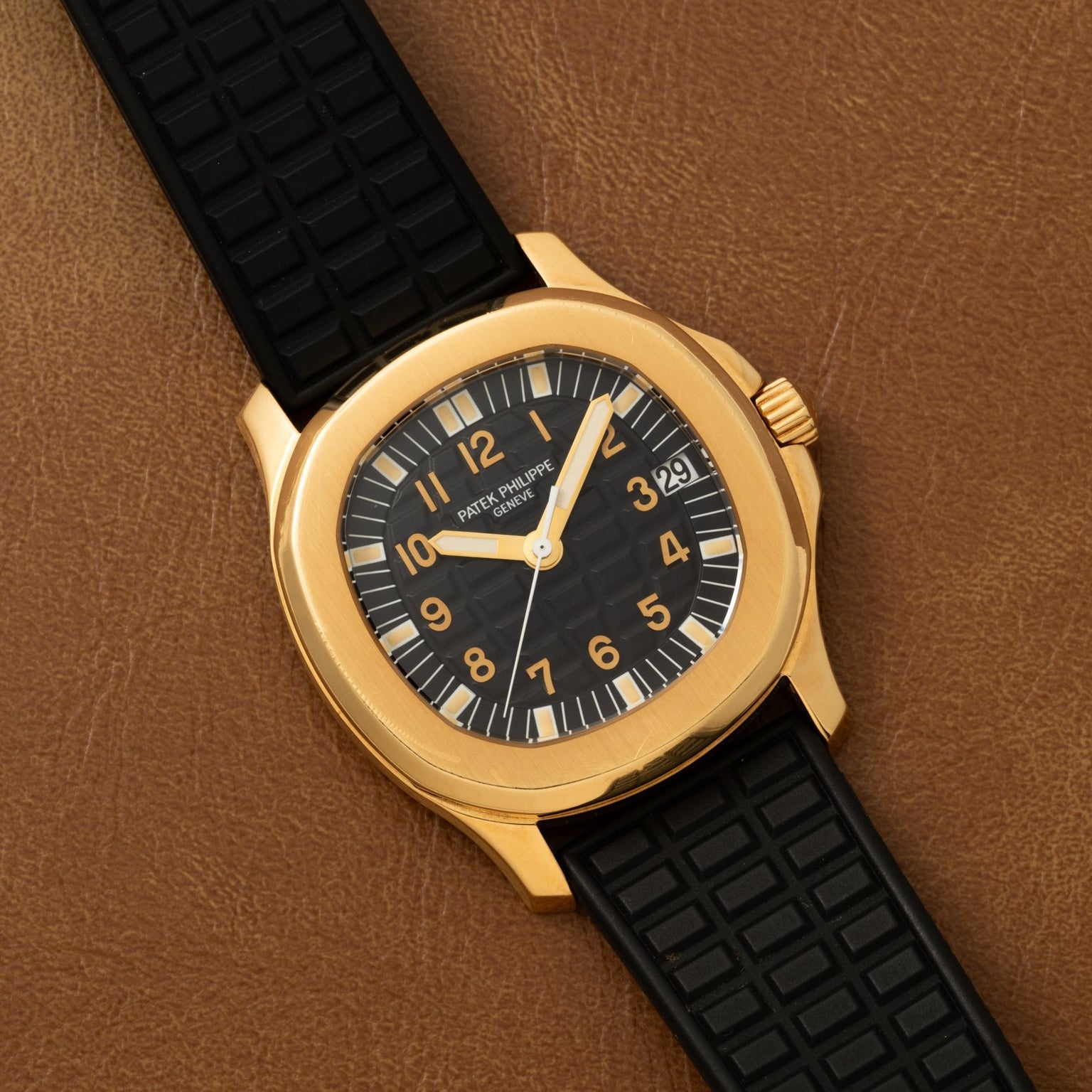 Patek Philippe Aquanaut with a black dial and strap, displayed on a brown leather surface.