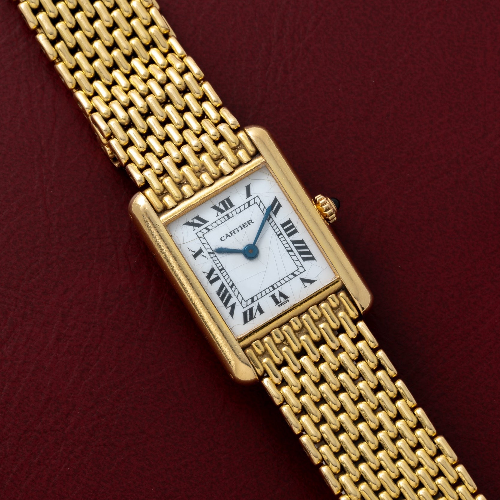 The Cartier Tank Louis wristwatch features a rectangular face with Roman numeral markers, set against a red leather surface.