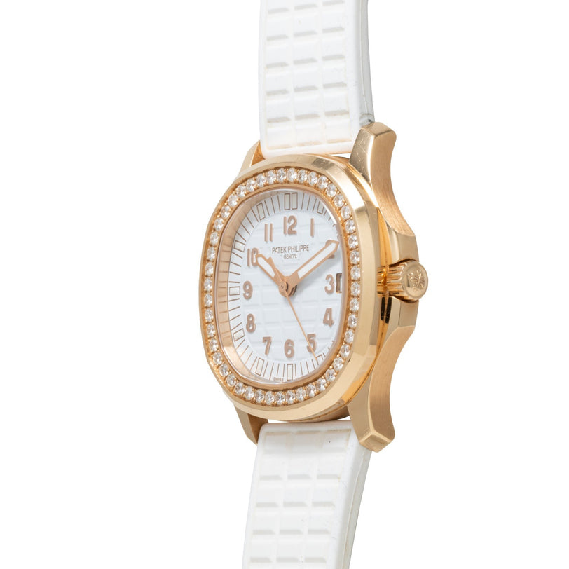 The Patek Philippe Aquanaut Ladies watch features a white face, diamond bezel, and white textured strap, shown in an angled photograph.