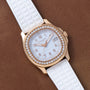 A Patek Philippe Aquanaut Ladies watch with a gold case, diamond bezel, and white strap displayed on a brown leather surface.