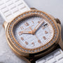 Close-up of the Patek Philippe Aquanaut Ladies watch, featuring a white strap and diamond-studded gold bezel, displayed on a marble surface.
