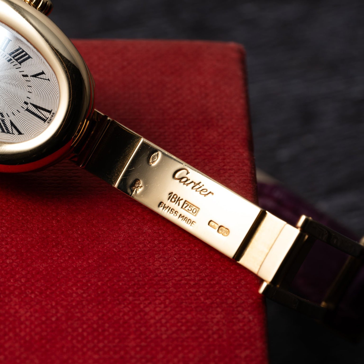 Close-up of a Cartier Baignoire gold watch band engraved with 18K, Swiss Made, and the Cartier logo.