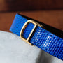 Close-up of Cartiers Tank Louis Diamonds watch featuring a blue textured leather strap and gold buckle, resting on a white marble surface.