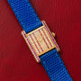 The Cartier Tank Louis Diamonds features a bejeweled face with diamonds and pink gemstones, a blue strap on red leather, and a gold case.