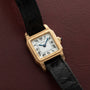 The Cartier Santos Mini watch with a black leather strap rests on a textured dark red surface.