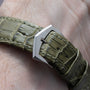Close-up of a green alligator leather strap with a silver buckle on a wrist, featuring the Patek Philippe Calatrava Cloisonné Tropical Leaves II watch.