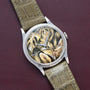 The Patek Philippe Calatrava Cloisonné Tropical Leaves II features a leaf-patterned face and olive green leather strap, showcased against a burgundy background.