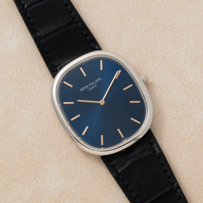A Patek Philippe Ellipse Jumbo watch with a blue dial and black leather strap rests on a light beige surface.