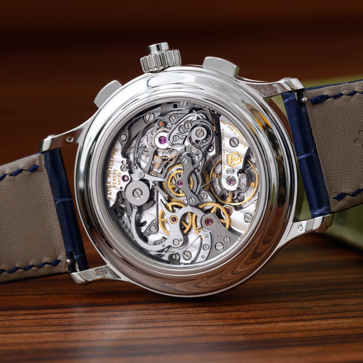 The Patek Philippe Split-Seconds Chronograph, a luxury watch with an exposed intricate mechanical movement and blue leather strap, rests on a wooden surface.