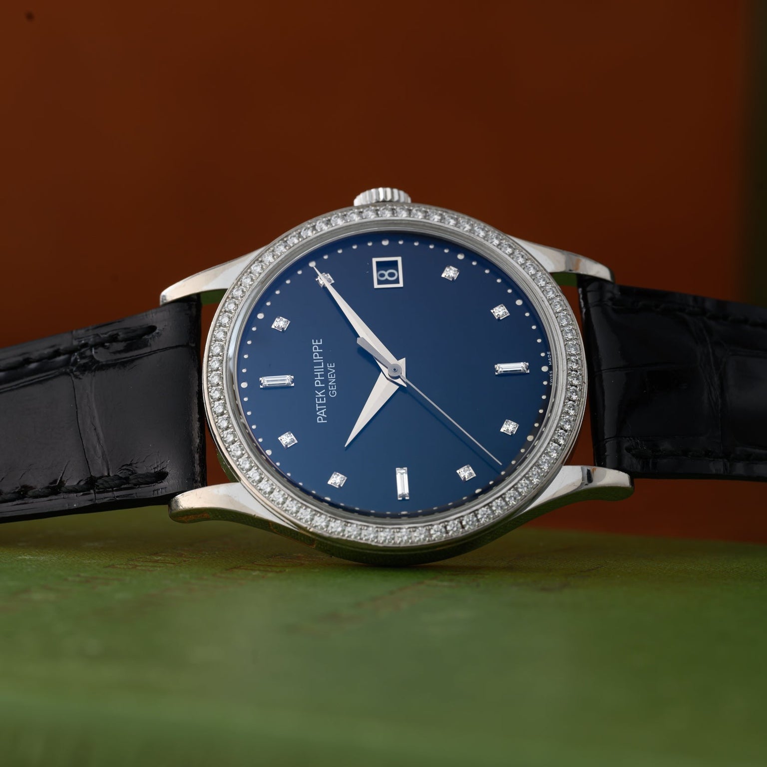 The Patek Philippe Calatrava Diamond Bezel, featuring a blue face, diamond markers, and a black leather strap, rests on a green surface.