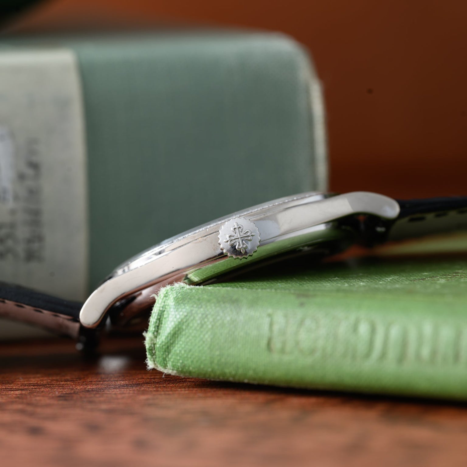 A close-up side view of the Patek Philippe Calatrava Diamond Bezel wristwatch in silver, resting on a green hardcover book.