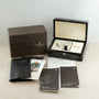A Patek Philippe Annual Calendar Moonphase watch in white gold, presented with a brown box, wooden case, pen, key, black booklet holder, and several instruction and certificate booklets on a light surface.