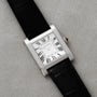 The Cartier Tank Normale watch features a rectangular case, black leather strap, and Roman numeral dial, displayed on a light gray surface.
