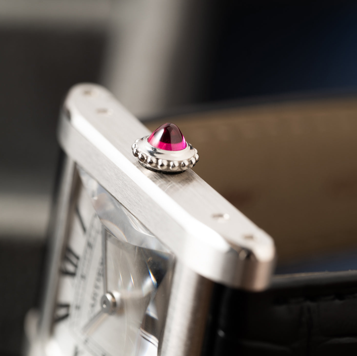 Close-up of the Cartier Tank Normale’s crown, adorned with a red gemstone, revealing part of the watch face and leather strap.