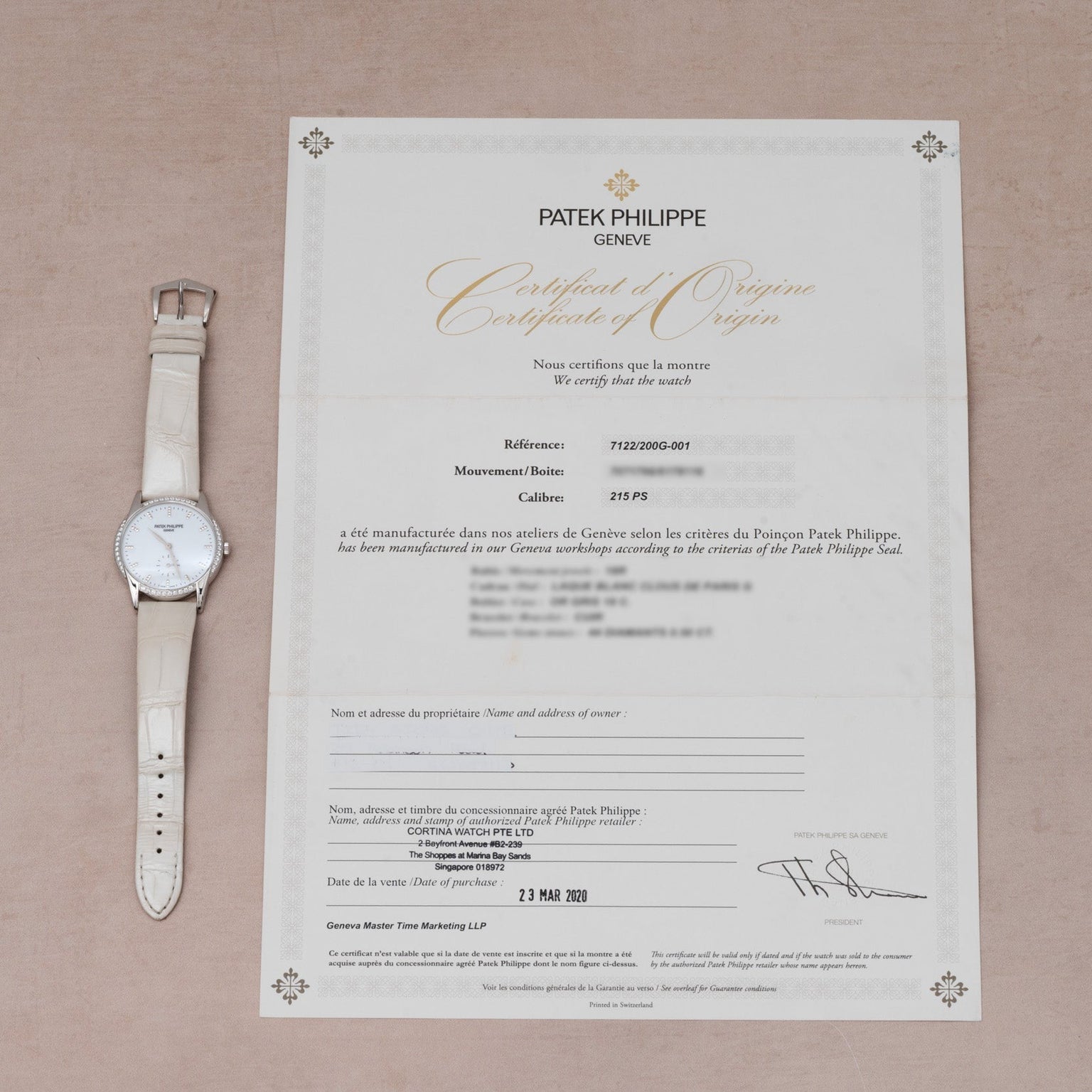 A white Patek Philippe Calatrava wristwatch rests next to its certificate of origin on a beige surface.