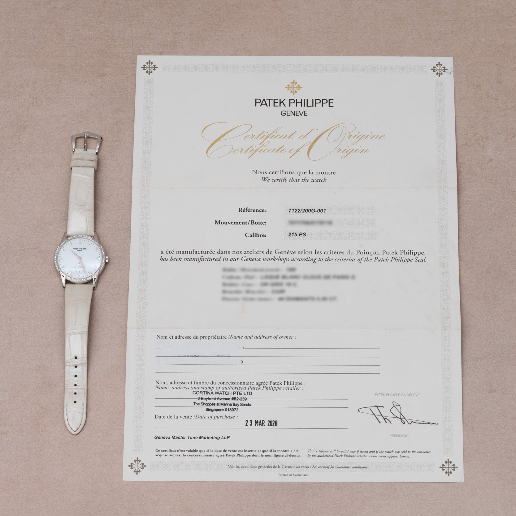 A white Patek Philippe Calatrava wristwatch rests next to its certificate of origin on a beige surface.