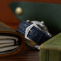 A close-up of the Patek Philippe Calatrava, featuring a blue leather strap and diamond-studded buckle, resting on books.