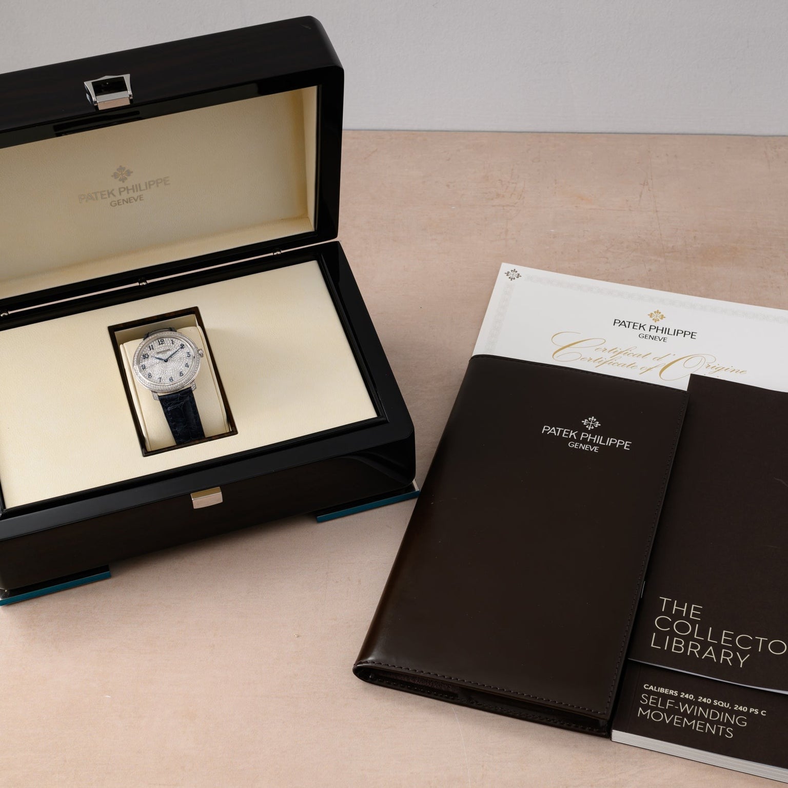 A Patek Philippe Calatrava in its box, accompanied by booklets, a certificate, and a brown leather folder.