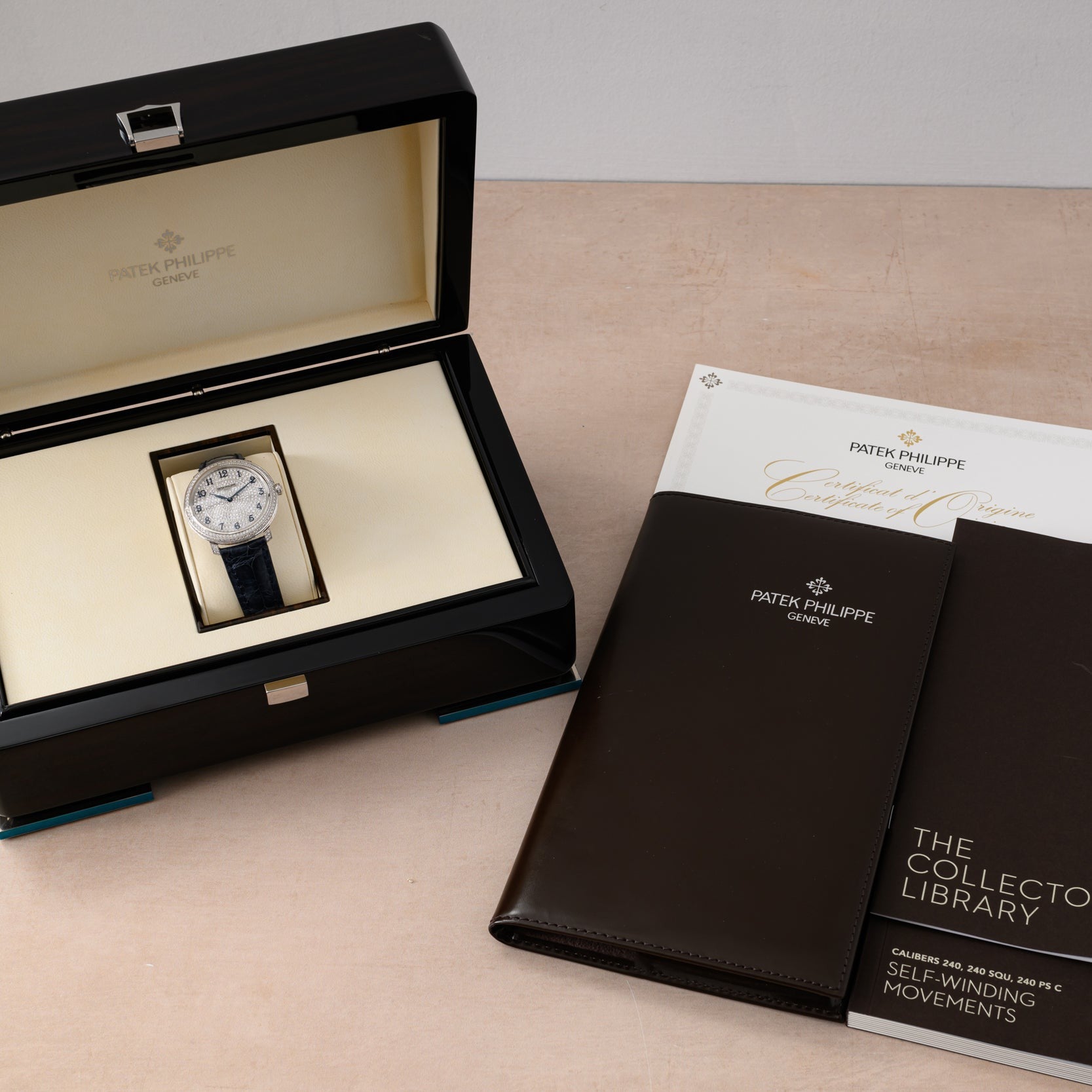 A Patek Philippe Calatrava in its box, accompanied by booklets, a certificate, and a brown leather folder.