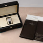 A Patek Philippe Calatrava in its box, accompanied by booklets, a certificate, and a brown leather folder.
