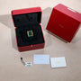 A Cartier Tank Louis watch in a red box, with tags, warranty card, and booklet arranged on a beige surface.