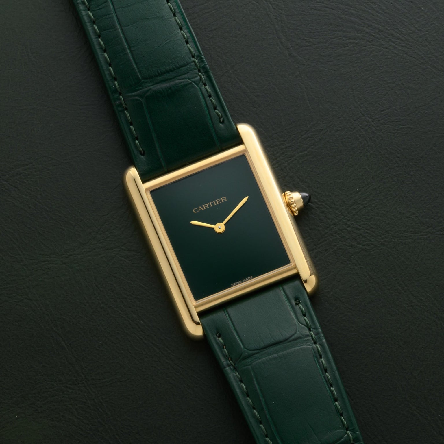 A Cartier Tank Louis watch with a gold case, green face, and green leather strap is displayed against a matching green background.