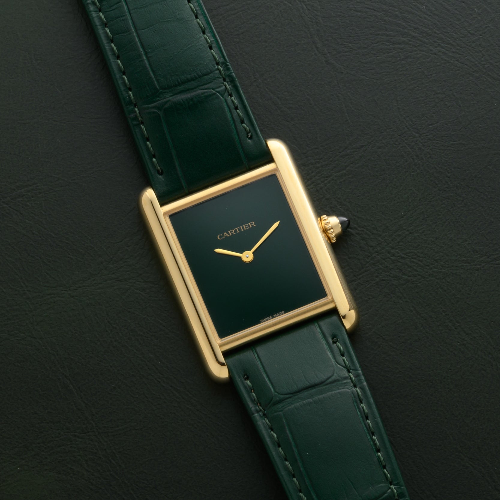 A Cartier Tank Louis watch with a gold case, green face, and green leather strap is displayed against a matching green background.