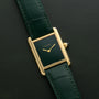 A Cartier Tank Louis watch with a gold case, green face, and green leather strap is displayed against a matching green background.