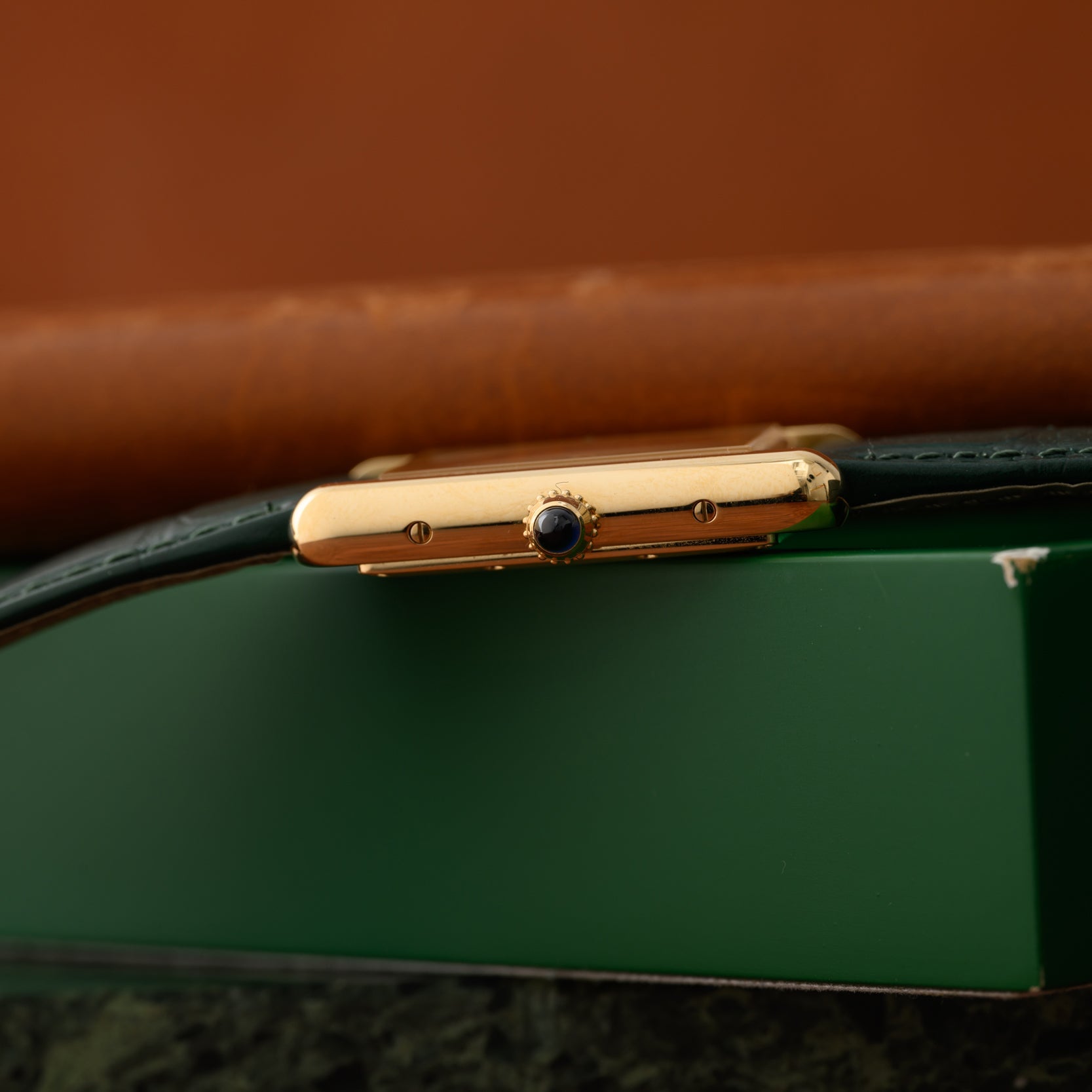 Close-up side view of the Cartier Tank Louis gold wristwatch with a dark crown, resting on a green surface.