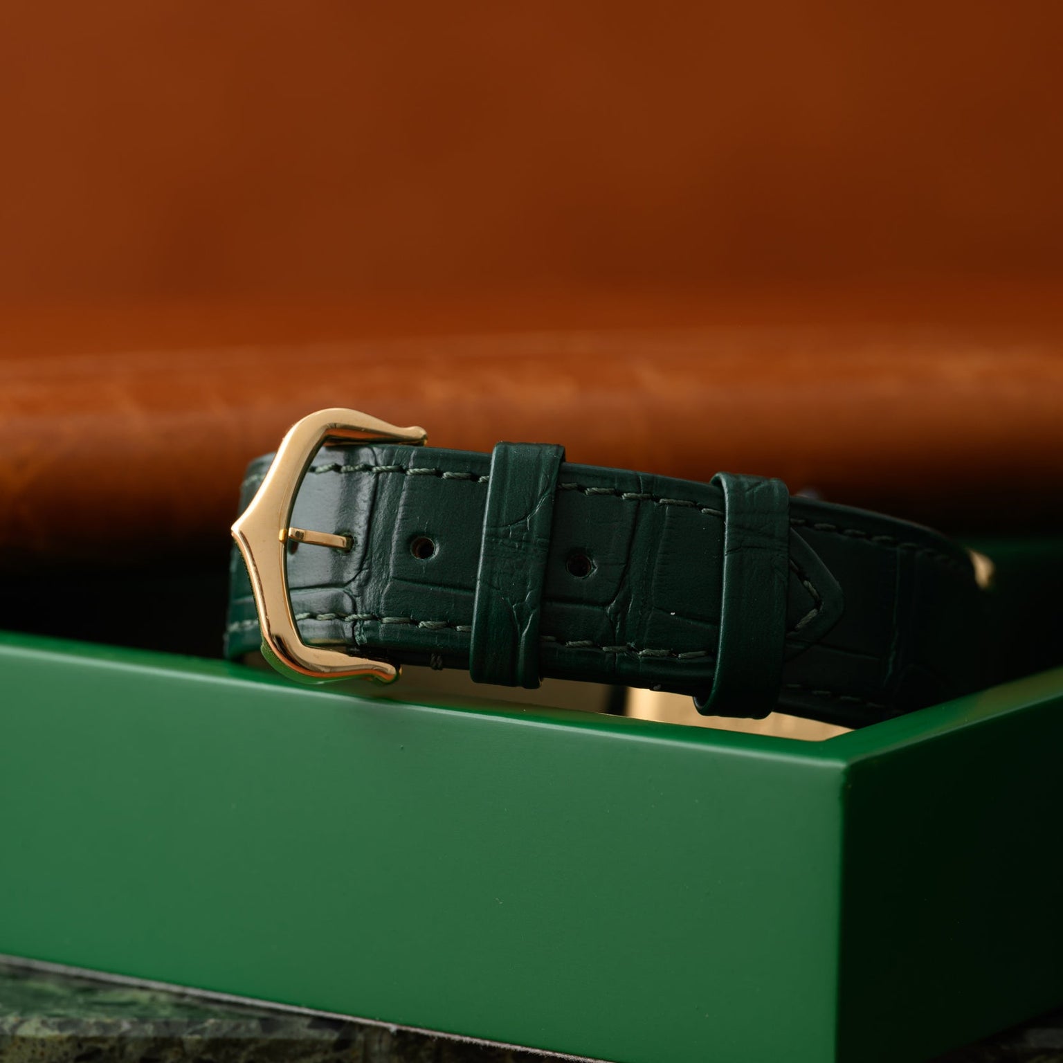 The Cartier Tank Louis green leather watch strap with a gold buckle rests on a matching green box.