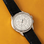 The Patek Philippe Multi-Scale Chronograph, featuring a black leather strap and an intricate white dial, is displayed on a yellow textured surface.