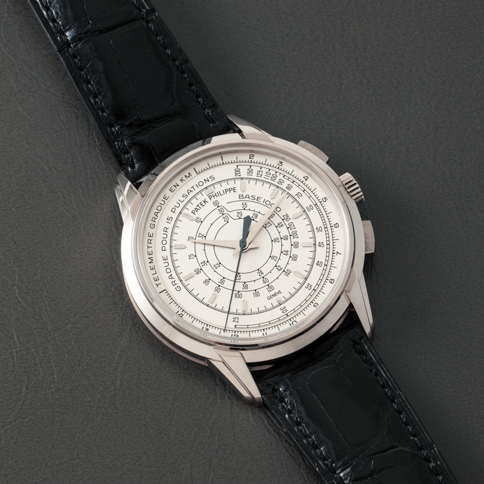 The Patek Philippe Multi-Scale Chronograph, featuring a black leather strap and intricate silver dial, is elegantly displayed on a dark surface.