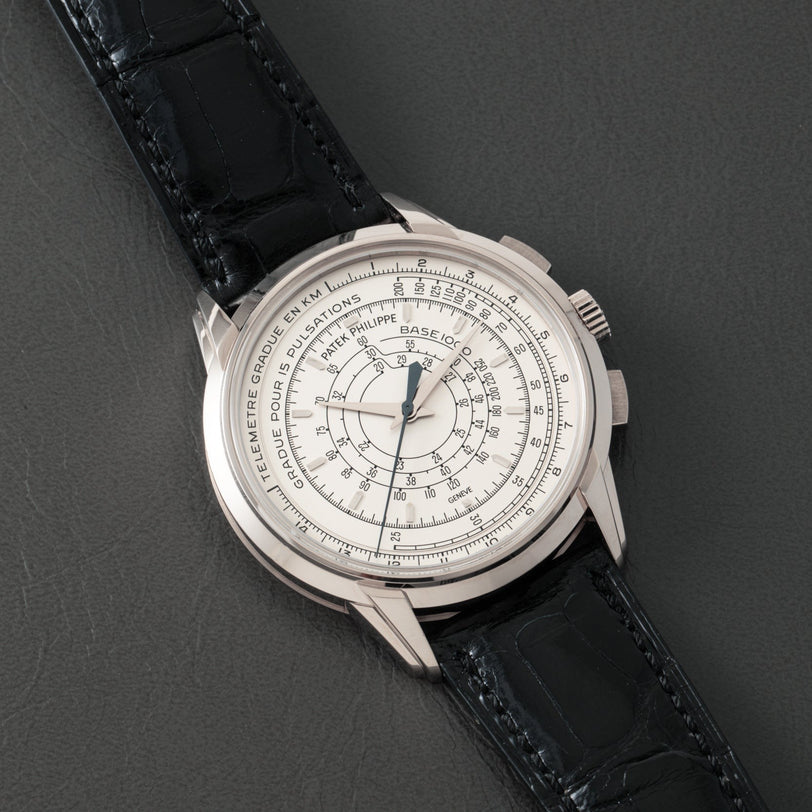 The Patek Philippe Multi-Scale Chronograph, featuring a black leather strap and intricate silver dial, is elegantly displayed on a dark surface.